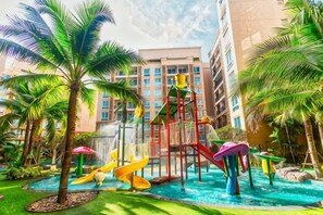 A hotel courtyard with a children's play area, palm trees, and a pool.