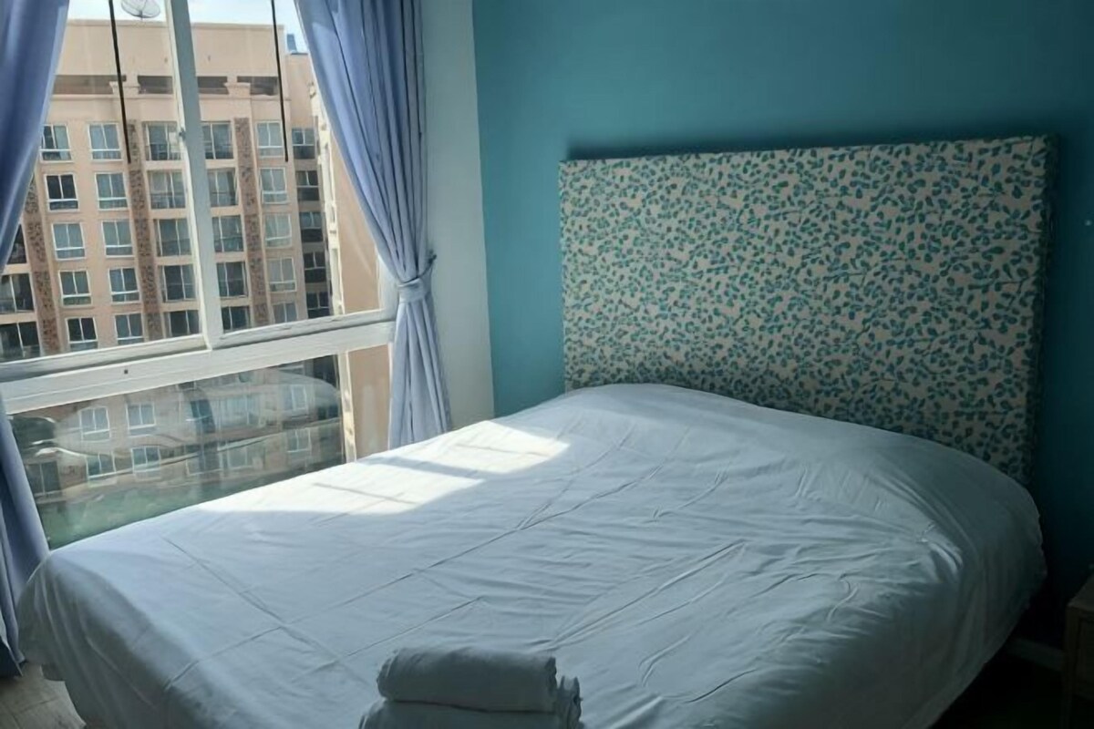 A bed with a white mattress and pillows, a patterned headboard, and a window with curtains.