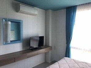 A hotel room with a bed, a TV on a wooden shelf, a small table, and a window with curtains. - Atlantis Condo Resort Jomtien by EVT (Pattaya)