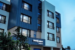 A multi-story building with balconies, a visible entrance, and a sign indicating a business or service area.