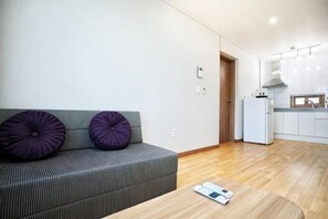 A modern living room with a grey sofa, purple cushions, a wooden coffee table, and a kitchen in the background. - The Naeun Stay (Seogwipo)