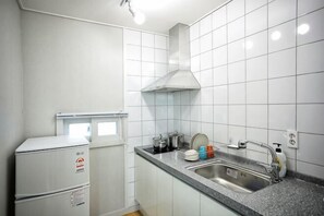 Uma cozinha com azulejos brancos, forno embutido, pia e bancada de aço inoxidável.