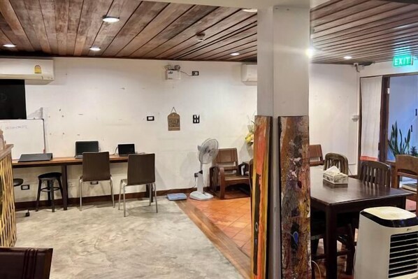 Una habitación con techo de madera, una pizarra, varias mesas con computadoras, sillas y un ventilador.