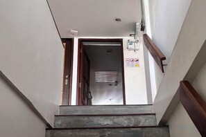 Een smalle trap met een houten leuning, een metalen balustrade, en een deur aan de bovenkant die naar een kamer leidt.