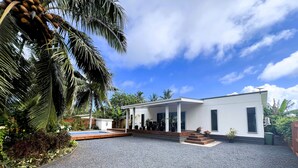 Une maison moderne dotée d’un porche abrité, d’une piscine et d’une allée en gravier.