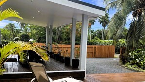Un espace extérieur abrité doté d’un plancher en bois, de deux fauteuils de relaxation, d’une piscine et d’une végétation luxuriante.