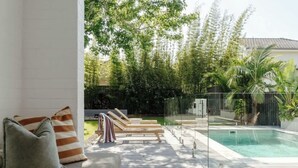 Un espace aménagé au bord de la piscine, avec une terrasse en bois, des chaises longues et une piscine entourée de parois en verre.