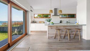 Una cocina moderna con ventanas amplias, una isla central con taburetes y vistas al exterior.