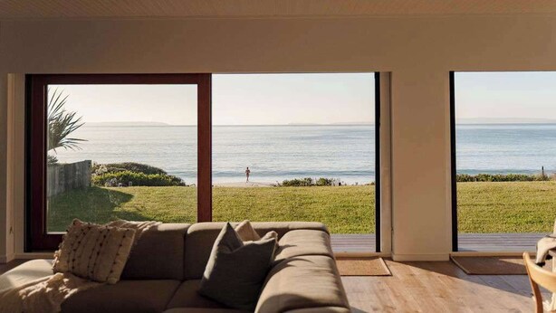 Una sala de estar moderna con un amplio ventanal corredera que da a un balcón con vistas al mar.