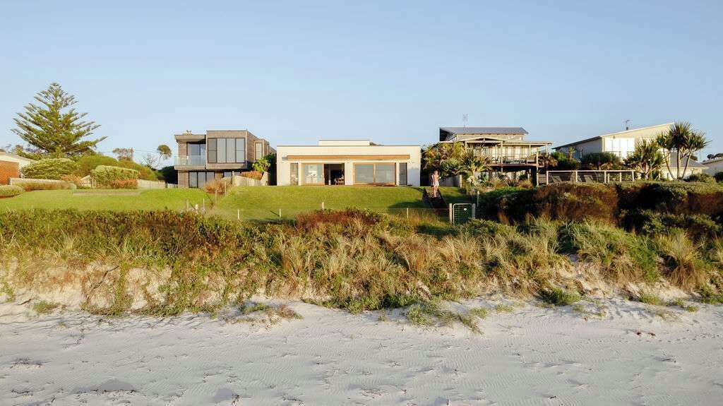 Una proprietà sul lungomare con case moderne, una spiaggia sabbiosa e dune erbose.