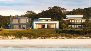 Una propiedad frente a la playa con arquitectura moderna, que presenta una casa grande con techo plano y ventanas amplias, ubicada en una playa de arena con aguas turquesas cristalinas.