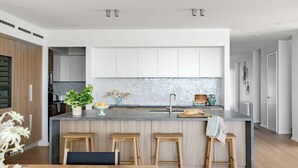 A modern kitchen with a central island, wooden stools, and a white backsplash.
