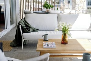 Un espace de détente extérieur moderne, avec un canapé blanc, une table basse en bois et un vase rempli de fleurs blanches.