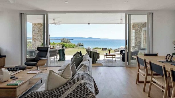 A modern living room with a large glass door leading to a balcony overlooking the sea.