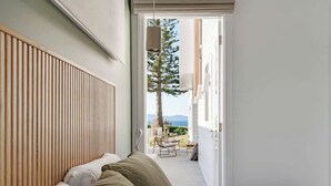 A bedroom with a large window, a wooden headboard, and a view of a balcony with outdoor furniture.