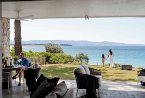 Une terrasse extérieure avec vue sur la mer, des piliers en pierre et une table entourée de chaises.