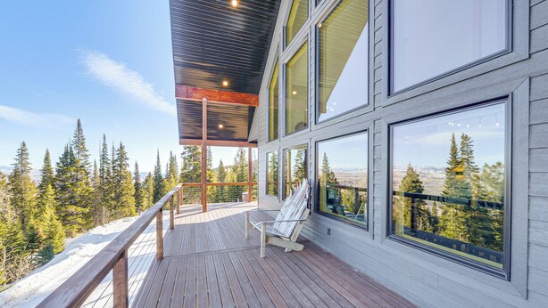 A wooden deck with a chair, large windows, and a view of trees and mountains. - Views, Trails, Hot Tub & More: Luxe Wyoming Oasis (Dubois)
