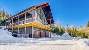 A modern two-story building with large windows and a balcony, surrounded by snow and trees. - Views, Trails, Hot Tub & More: Luxe Wyoming Oasis (Dubois)