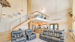 A spacious living area with a large leather sofa, a wooden staircase, and a kitchen in the background. - Views, Trails, Hot Tub & More: Luxe Wyoming Oasis (Dubois)