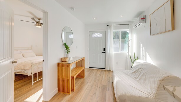 A room with a bed, a wooden bench, a table with a plant, and a door leading to another room. - 35 Mi to LA: Modern Apartment in Chino! (Chino)