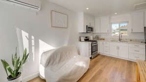 A modern kitchen with white cabinets, a microwave, and a stove. There is a white sofa and a potted plant in the corner. - 35 Mi to LA: Modern Apartment in Chino! (Chino)
