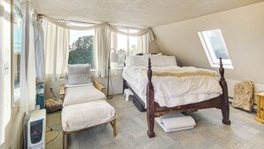 Un dormitorio con una cama grande, una mesita de noche, una silla, un calentador y una ventana con cortinas.