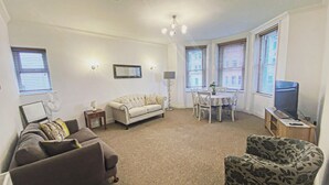 A living room with a sofa, armchair, dining table, and TV. - LUXURY 2 BED APARTMENT BY THE SEA (Bournemouth)