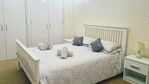 A bedroom with a bed, a nightstand, a lamp, a wardrobe, and a mirror. - LUXURY 2 BED APARTMENT BY THE SEA (Bournemouth)