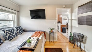 Une chambre moderne avec un lit, une télévision, une petite table avec une plante et une vue sur la cuisine.