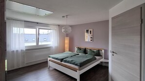 A bedroom with a bed, a window with curtains, a radiator, and a door. - Vacation home Ewergass in Mertesdorf - only 8 km from Trier + public transport ticket from 04-26 (Mertesdorf)