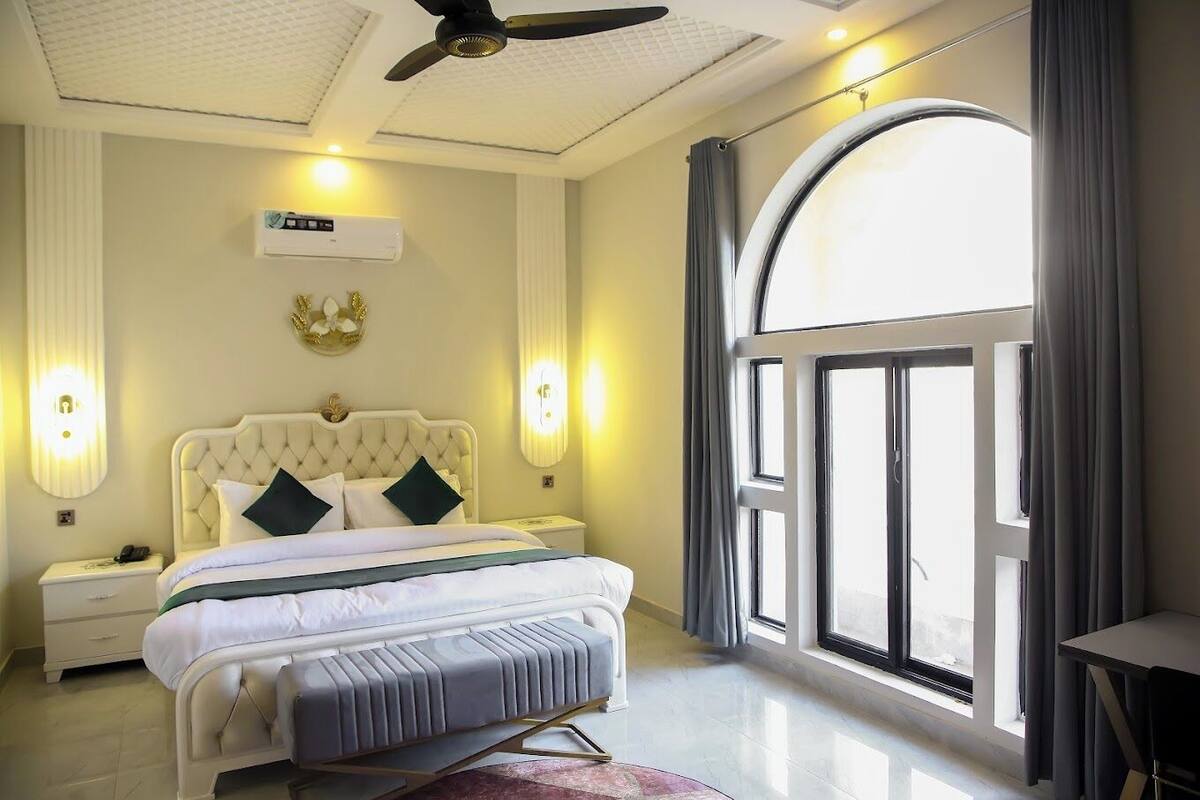 A bedroom with a large bed, a ceiling fan, a window with curtains, and a bedside table with a lamp.