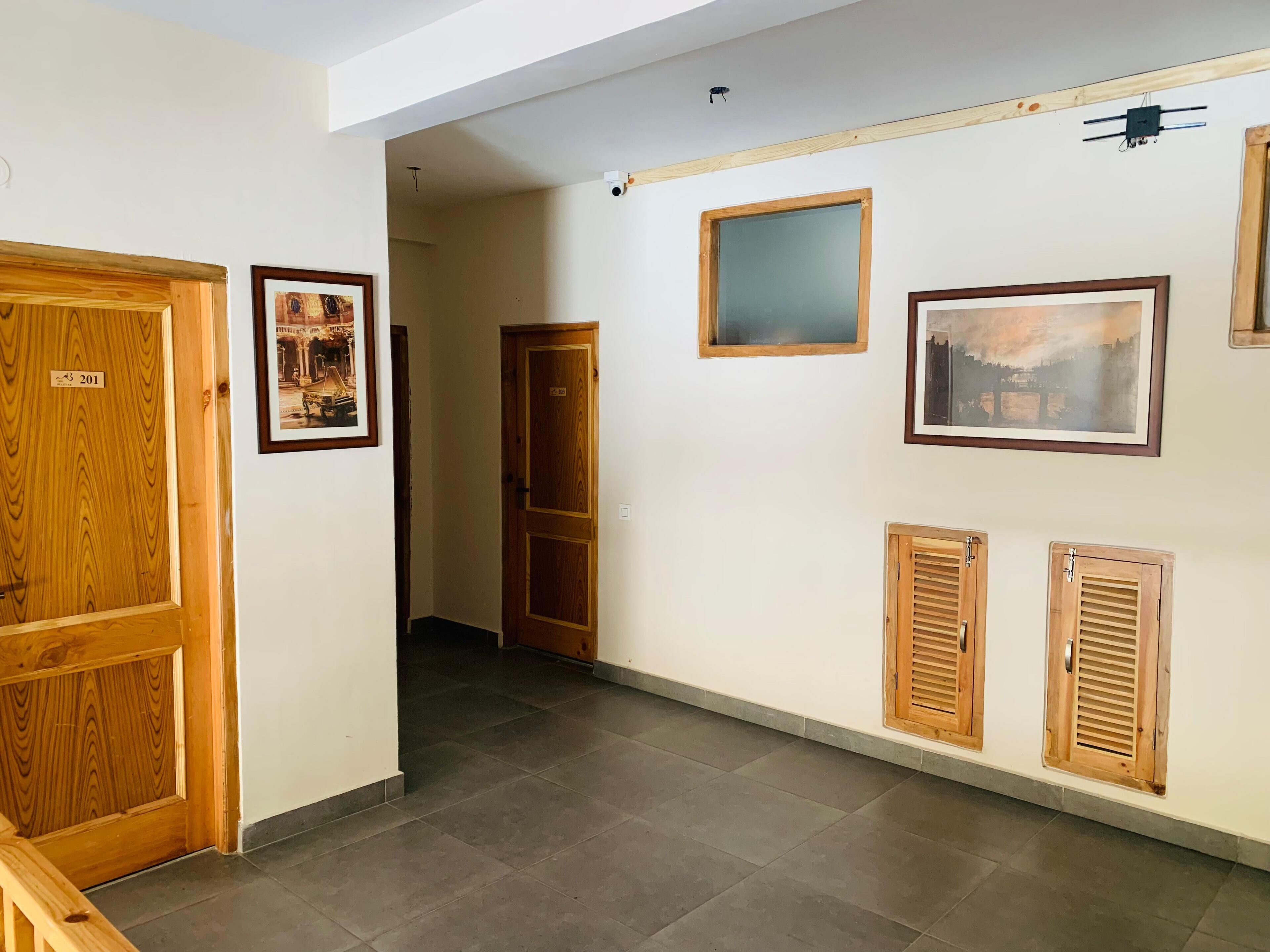 A hallway with wooden doors, framed pictures on the walls, and a tiled floor.