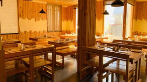A restaurant with wooden tables and benches, hanging pendant lights, and large windows allowing natural light. - The Bulevar-Whispering Willow (Lahul)