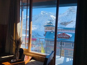 Una habitación con un amplio ventanal que ofrece vistas a montañas cubiertas de nieve y un edificio con techo azul.