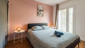 Ein Schlafzimmer mit Bett, Nachttischlampe, Wandbild und einem Fenster mit Vorhängen.