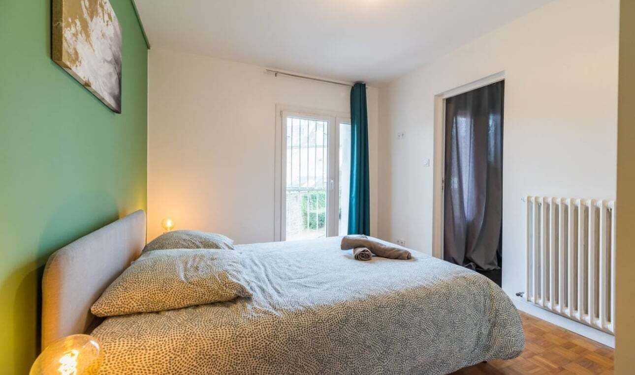 Ein Schlafzimmer mit einem Bett, einem Heizkörper, einem Fenster mit Vorhängen und einer Tür.
