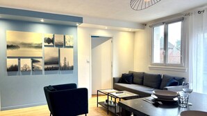 Ein modernes Wohnzimmer mit einer Couch, einem Sessel, einem Esstisch mit Tellern und Gläsern sowie einer Wand mit gerahmten Bildern.