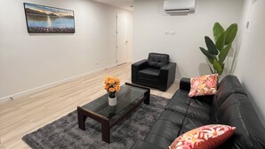 Ein modernes Wohnzimmer mit einer schwarzen Ledersofa, einem Glastisch mit Blumenvase, einem schwarzen Sessel und einem großen Fenster mit Bergblick.