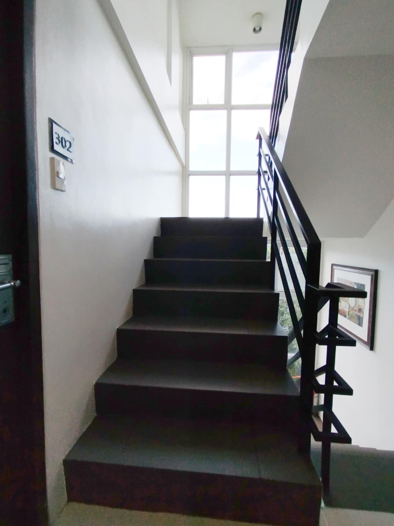 Un escalier avec une main courante noire mène à un palier. Une porte portant le numéro 302 est visible sur la gauche.