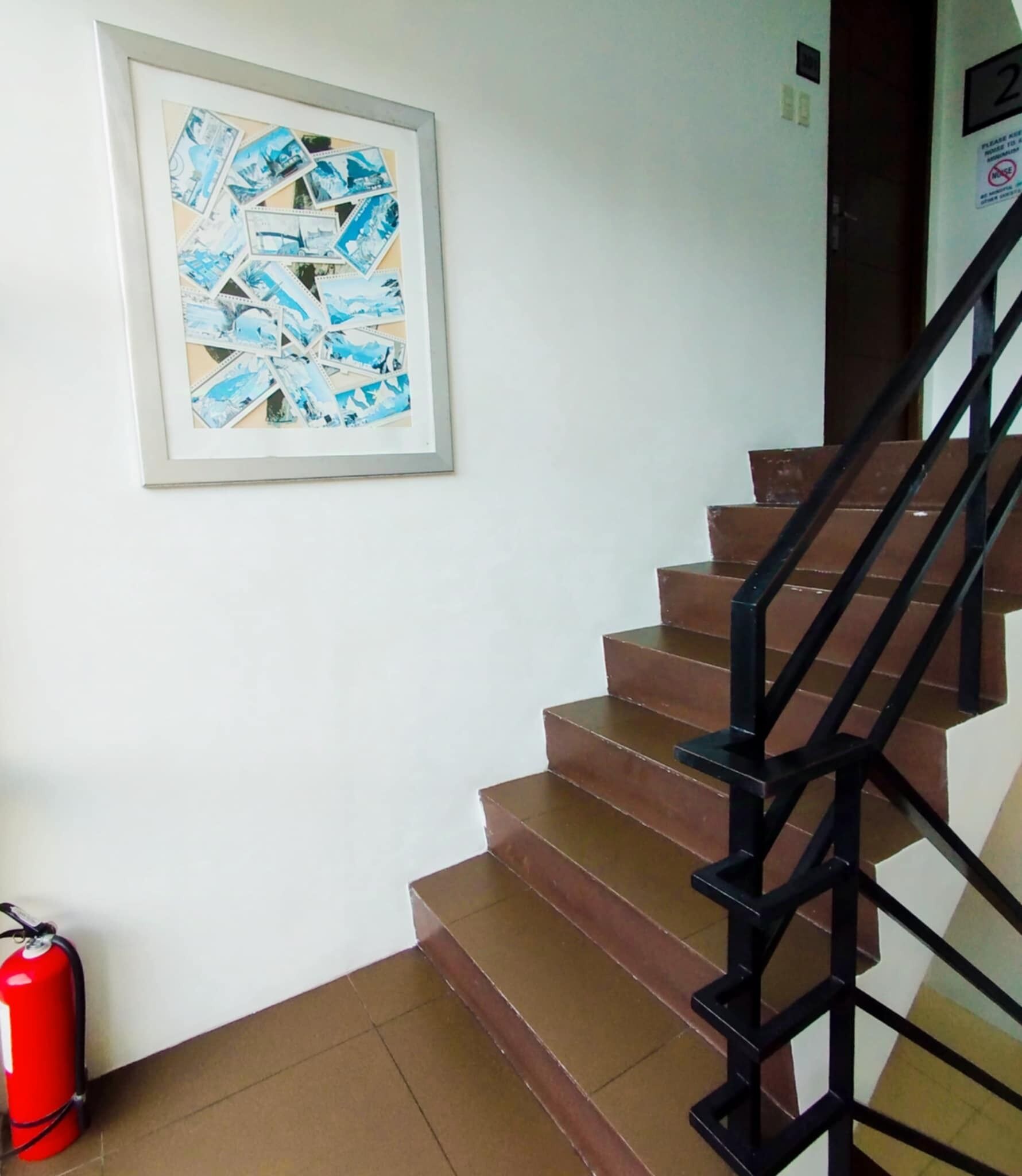 Una escalera con barandilla negra y un collage enmarcado de fotografías azules y blancas en la pared.