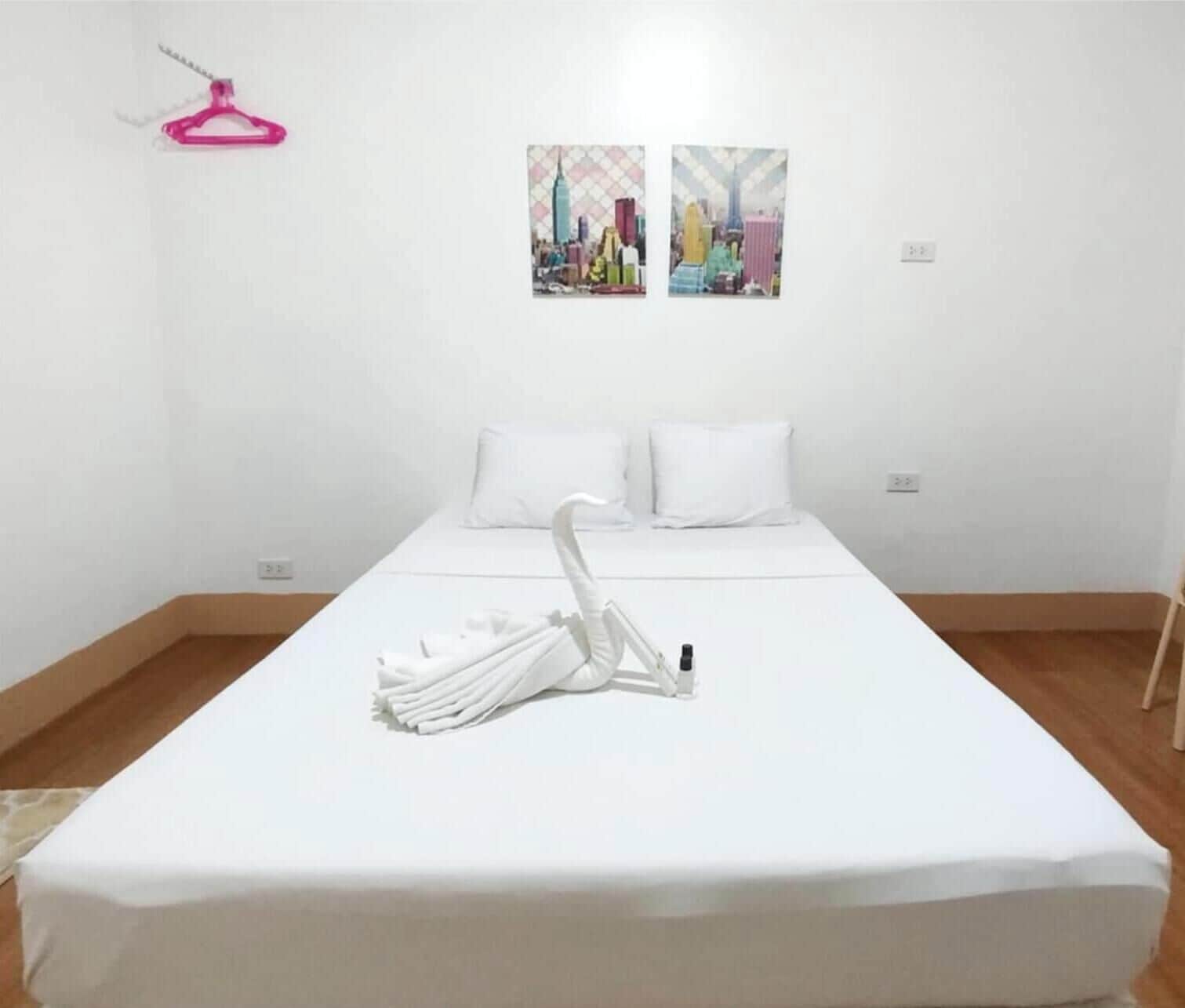 A hotel room with a bed, white pillows, a white towel, and two paintings on the wall.