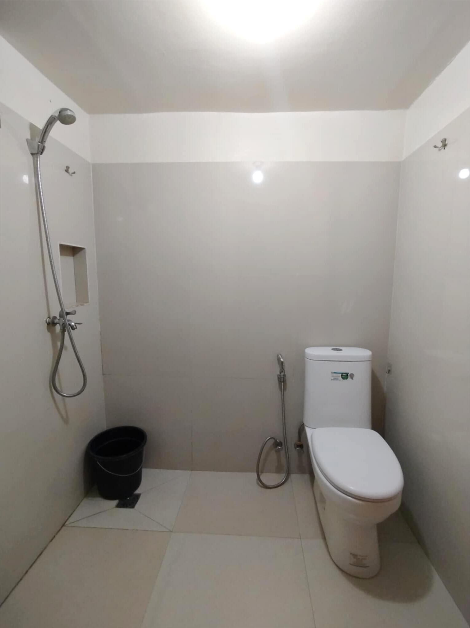 Un baño pequeño y funcional con inodoro, ducha y un cubo negro.