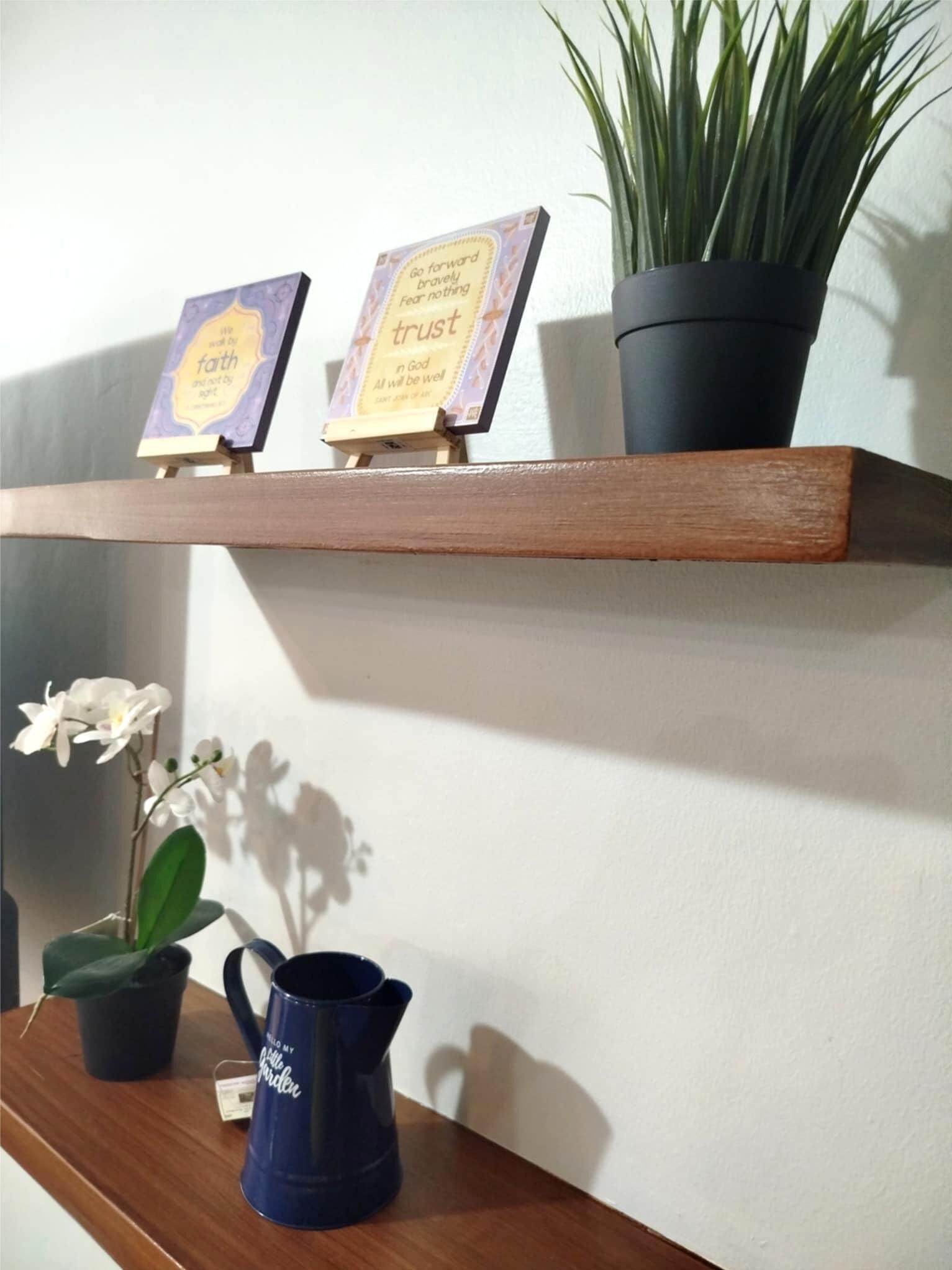 Een plank met twee ingelijste inspirerende citaten, een potplant, een blauwe gieter en een orchidee.