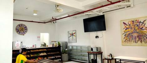A cafe with wooden benches, a clock, a TV, and a colorful painting.