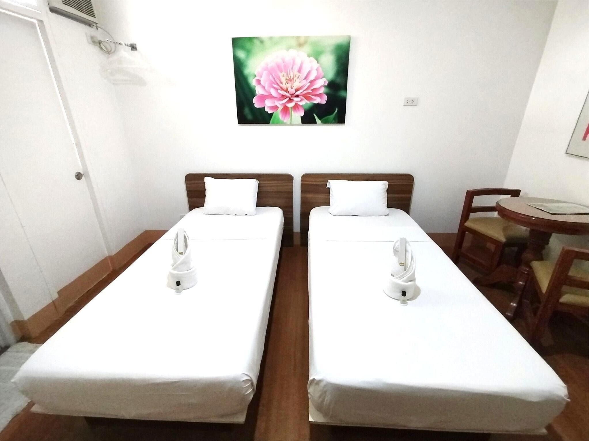 A hotel room with two single beds, a small table with chairs, and a painting of a flower on the wall.