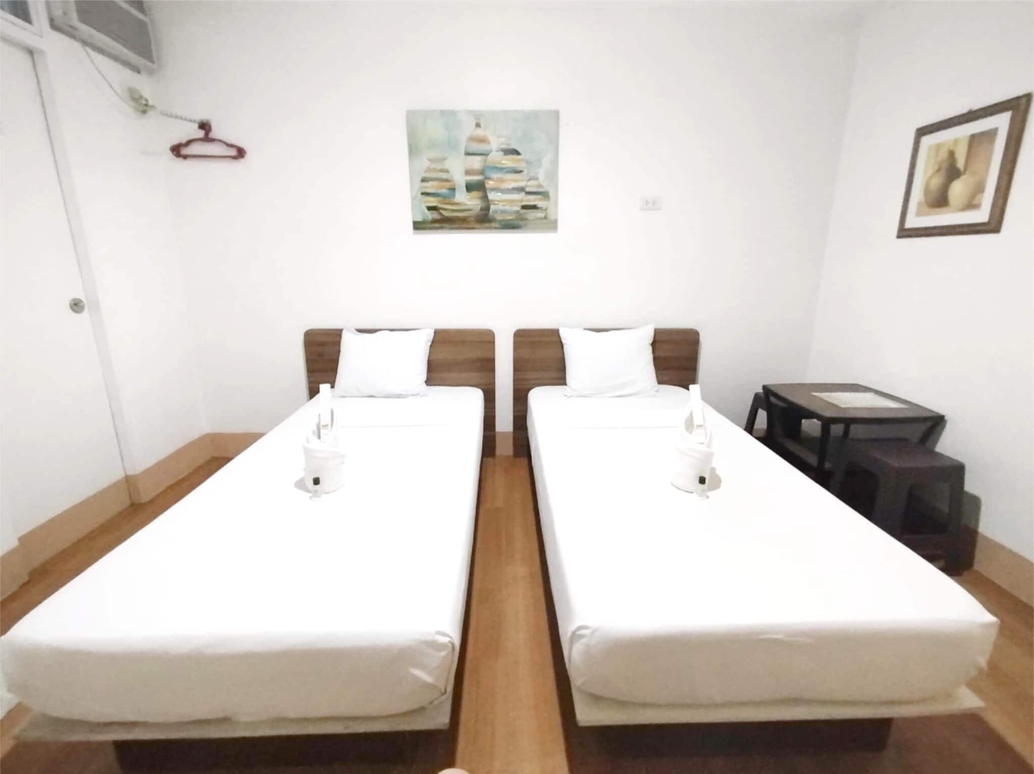 Hotellihuone, jossa on kaksi erillistä sänkyä, pieni pöytä ja taulu seinällä.