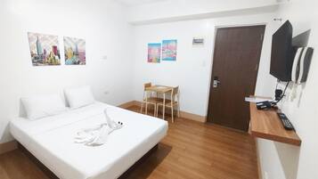 A hotel room with a bed, a desk, a chair, a TV, and artwork on the walls.