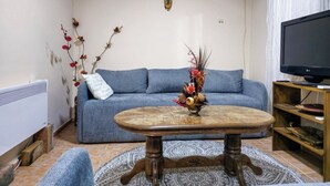 Una sala de estar con un sofá azul, una mesa de centro de madera, un televisor y un jarrón decorativo.
