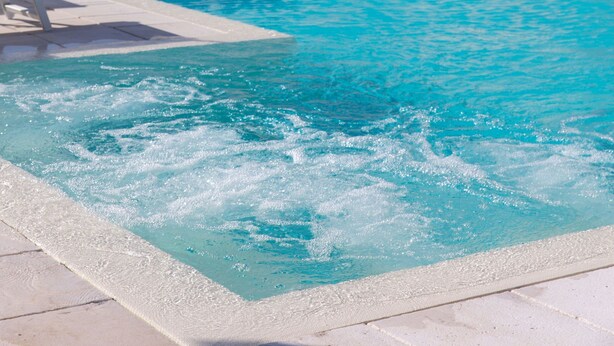 Una piscina con sillas de descanso y sombrillas, rodeada por un edificio moderno con balcones.