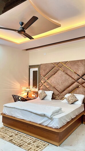 A bedroom with a bed, a ceiling fan, a nightstand, and a mirror. - shree laxmi palace (Nivari)